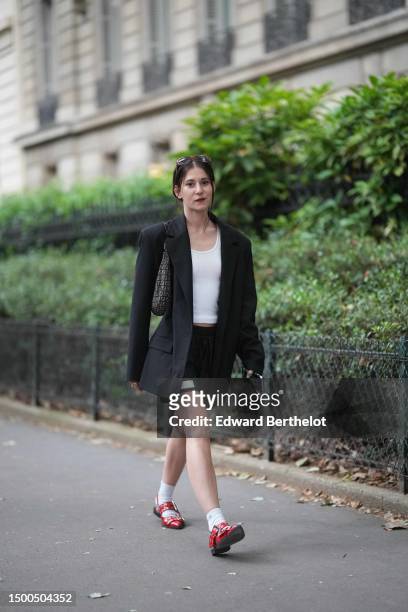 Guest wears a white tank-top, a black oversized blazer jacket, black nylon with large white straps pattern shorts from GCDS, a black and gray FF...