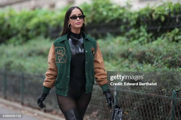 Guest wears black sunglasses, silver earrings, a black shiny vinyl turtleneck body, a dark green felt and brown suede sleeves buttoned teddy coat...