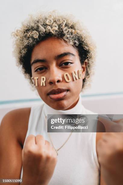 portrait of a young adult woman with the word "strong" made with stickers on her face - girl power stickers stock pictures, royalty-free photos & images