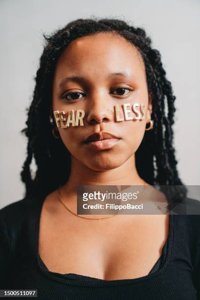 portrait of a young adult woman with the word "fearless" made with stickers on her face - girl power stickers stock pictures, royalty-free photos & images