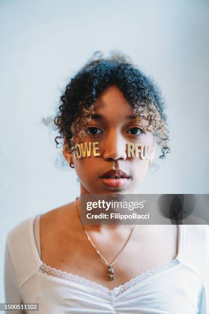 portrait of a young adult woman with the word "powerful" made with stickers on her face - girl power stickers stock pictures, royalty-free photos & images