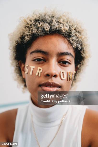 portrait of a young adult woman with the word "strong" made with stickers on her face - girl power stickers stock pictures, royalty-free photos & images