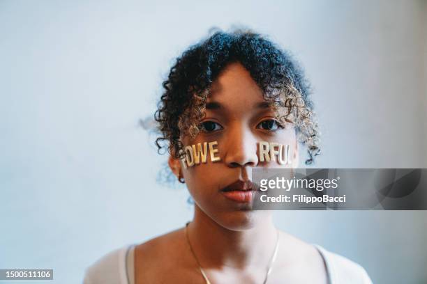 portrait of a young adult woman with the word "powerful" made with stickers on her face - girl power stickers stock pictures, royalty-free photos & images