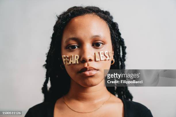 portrait of a young adult woman with the word "fearless" made with stickers on her face - girl power stickers stock pictures, royalty-free photos & images