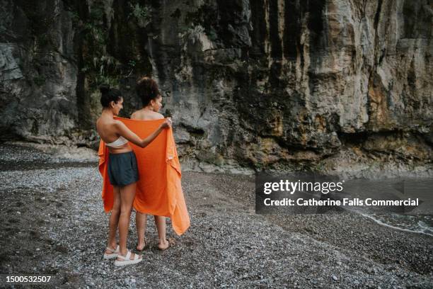 a woman holds a beach towel up, to protect her girlfriends modesty - surrounding support stock pictures, royalty-free photos & images