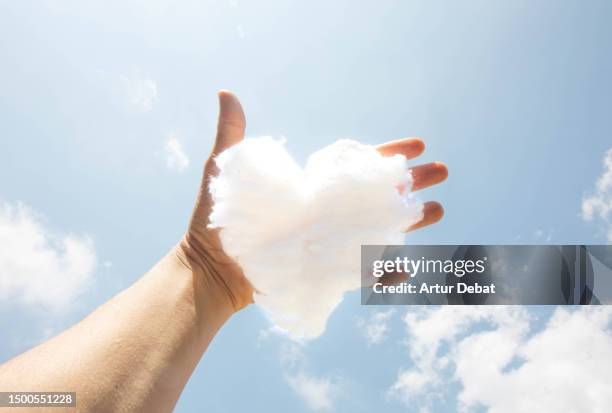 creative picture catching a cloud with heart shape from the sky with hand in personal perspective. - 位於中心 個照片及圖片檔