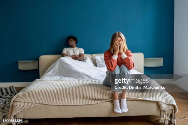 relationship breakdown between black guy and girl. sad woman sits on bed, covering face with hands - communication problems stock-fotos und bilder