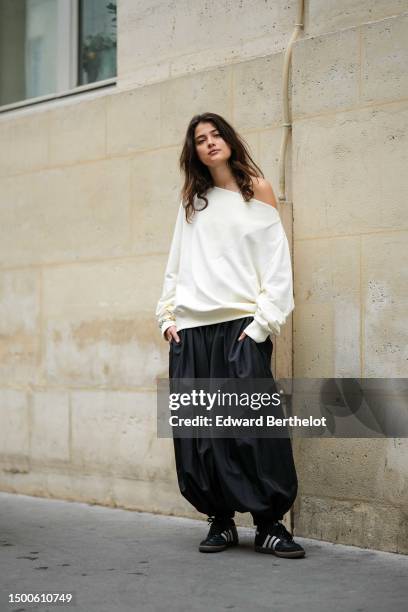 Guest wears a white latte asymmetric shoulder sweater, black puffy pants, black shiny leather with white strappy logo pattern leather sneakers from...