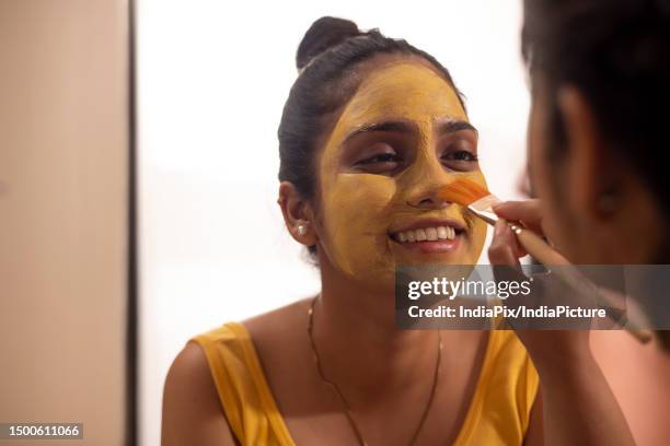 woman applying turmeric face pack on her friend's face - turmeric stock pictures, royalty-free photos & images