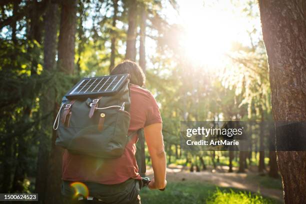 man with portable solar battery on his backpack to charge smartphone in nature while riding bicycle. sustainable lifestyle, ecological alternative energy and ecology concepts. - parque battery stock pictures, royalty-free photos & images