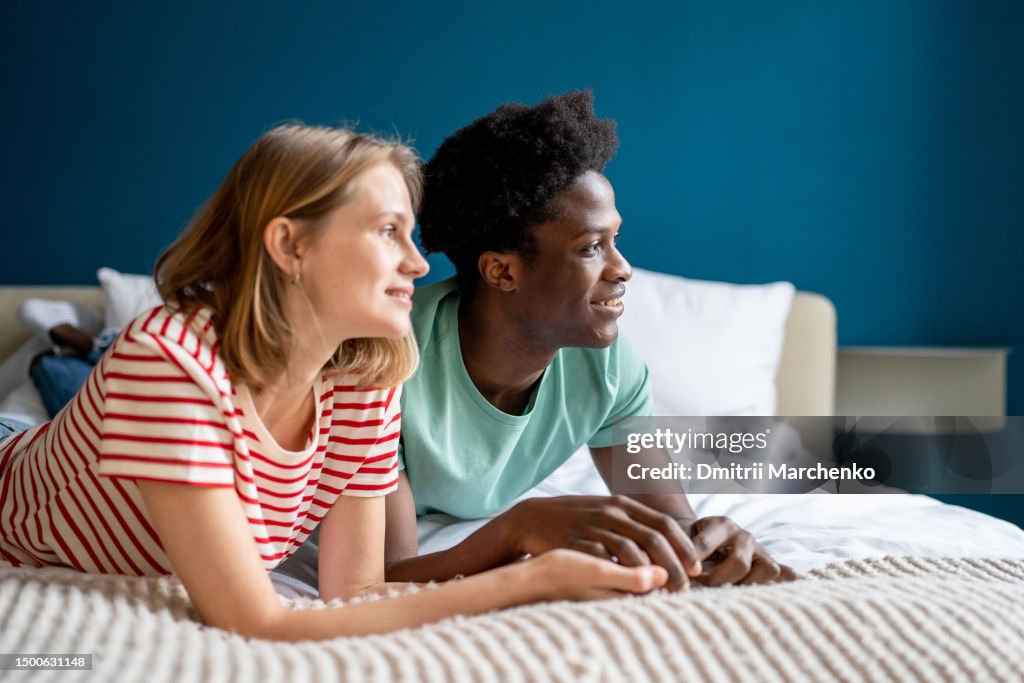 Happy carefree and smiling diverse couple lying on bed together. Interracial couple young woman and man