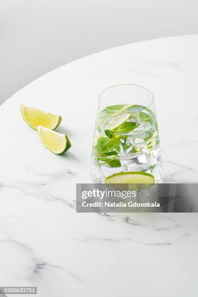 fresh summer lime and mint cocktail with ice cubes. drinking glass of soda drink. cold lemonade recipe. vitamin ready-to-eat mojito. sunlight, white marble table, still-life, lifestyle - gin tonic photos et images de collection