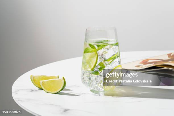 fresh summer lime and mint cocktail with ice cubes. drinking glass of soda drink. cold lemonade recipe. vitamin ready-to-eat mojito. sunlight, white marble table, still-life, lifestyle - gin stockfoto's en -beelden