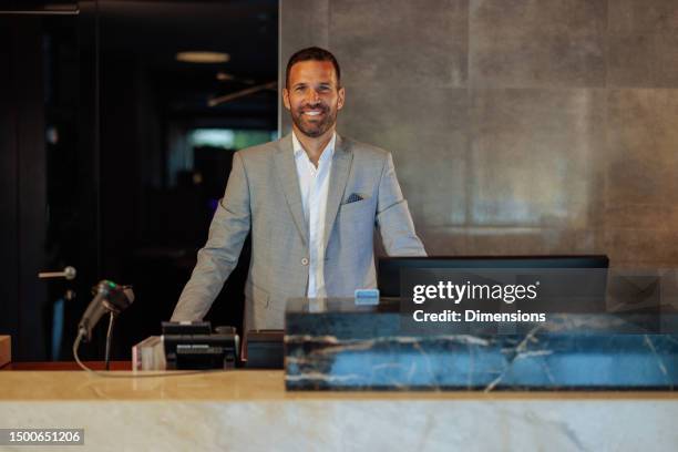 happy hotel receptionist standing behind counter - lobby stock pictures, royalty-free photos & images