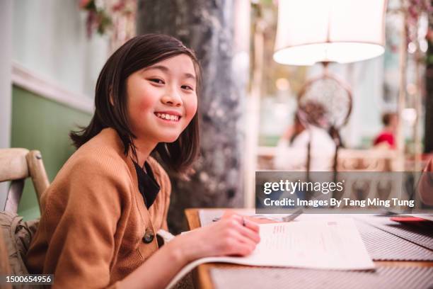 cheerful teenage girl smiling joyfully at the camera while looking at food menu in a restaurant - day in the life series fotografías e imágenes de stock