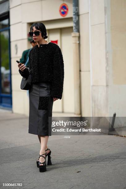 Guest wears black large sunglasses, a black fluffy jacket, a black midi dress, black shiny leather heels strappy shoes , outside Bluemarble, during...