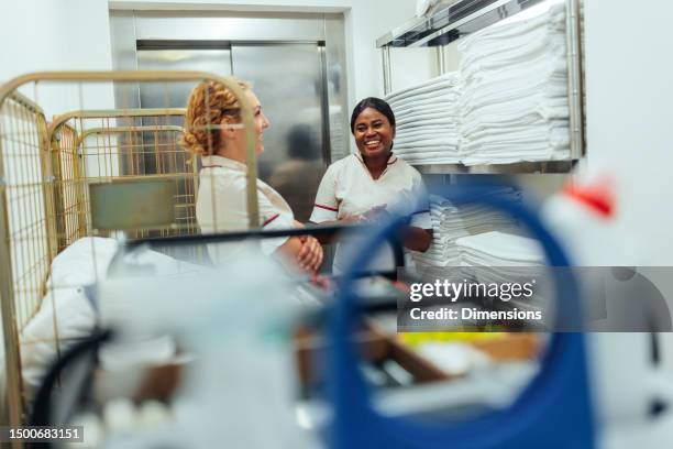 two diverse hotel maids laughing in laundry - hotel housekeeping stock pictures, royalty-free photos & images