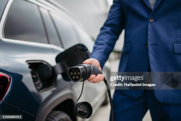 close up of businessman charging his electric car at charging station in front of his office. - enchufar fotografías e imágenes de stock