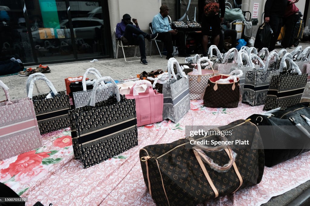 Knock-off luxury goods are displayed by sellers along a sidewalk