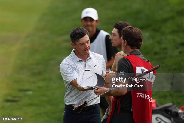 Rory McIlroy of Northern Ireland shakes hands with caddie Shay Knight as Viktor Hovland of Norway looks on from the 18th green during the first round...