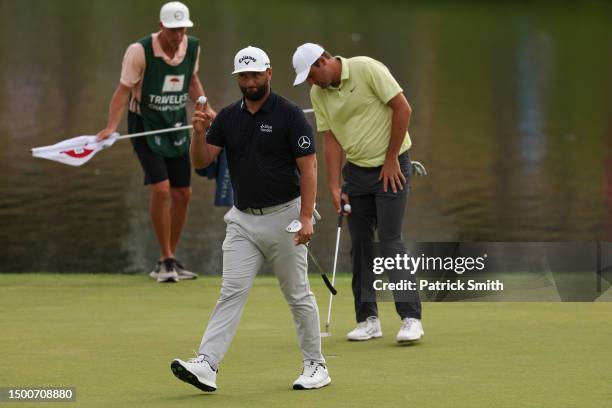 Jon Rahm of Spain waves as Scottie Scheffler of the United States and caddie Ted Scott look on during the first round of the Travelers Championship...