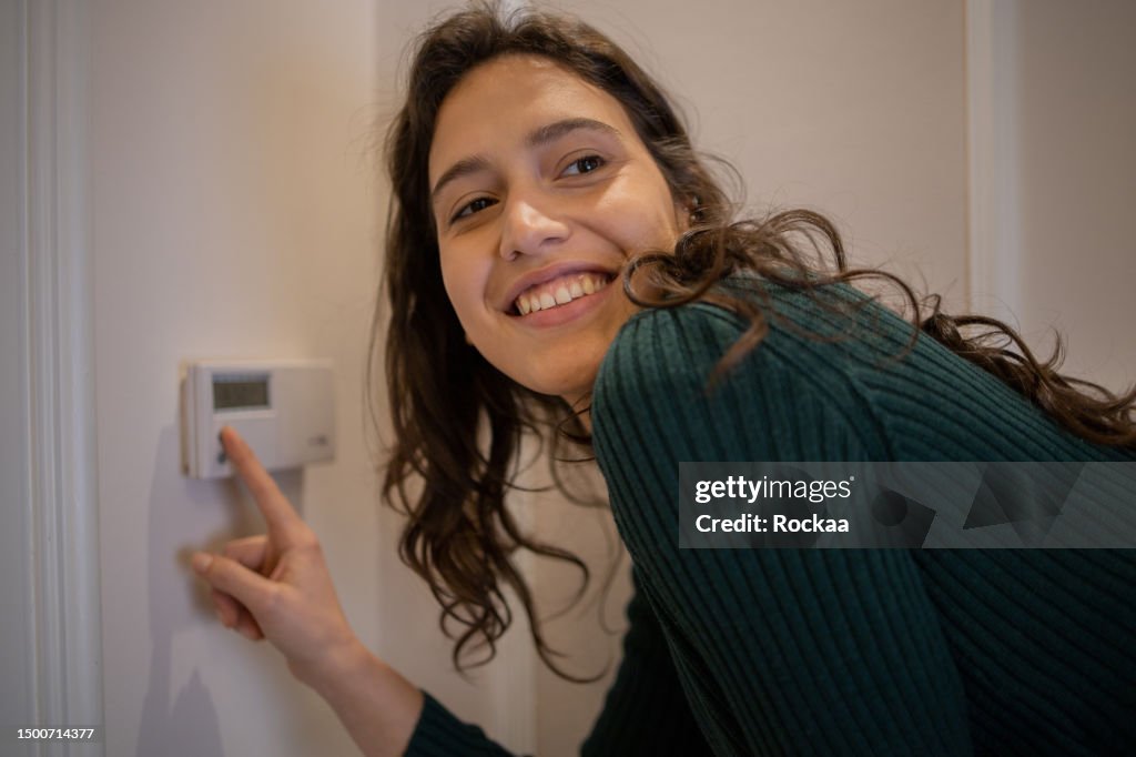 Young woman adjusts the temperature at home with a device on the wall