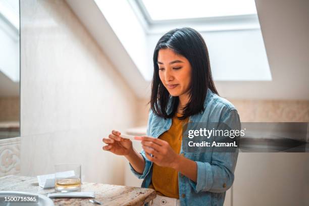 excited asian female performing pregnancy test at home - human fertility stock pictures, royalty-free photos & images