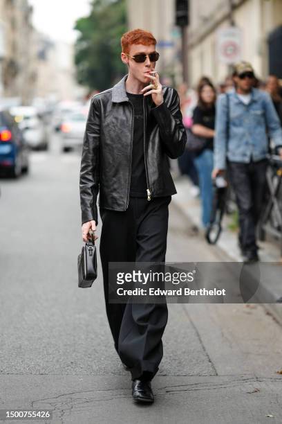Pierre Painchaud wears black sunglasses, silver earrings, gold rings, a black mesh / fishnet t-shirt, a black shiny leather zipper jacket, black...
