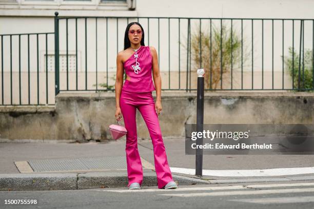 Aleali May wears pink futurist sunglasses, a rhinestones large butterfly pendant necklace, a neon pink asymmetric / shoulder-off / cut-out waist top,...