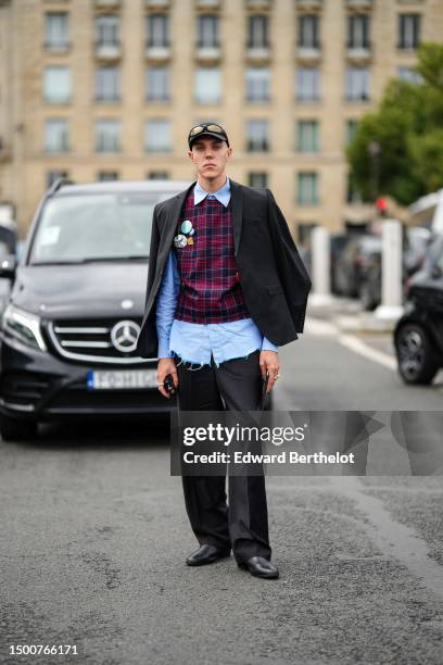 Guest wears a black cap, black sunglasses, a pale blue ripped shirt, a navy blue and burgundy checkered print pattern sleeveless breastplate...