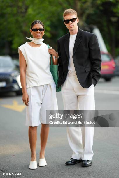 Guest wears black sunglasses, a white silk small scarf, a white sleeveless silk tank-top, a green shiny leather shoulder bag, white large suit...