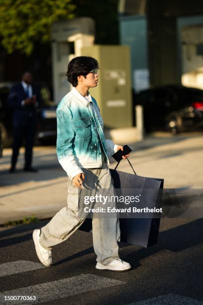 Guest wears a white t-shirt, a white and green tie and dye print pattern denim jacket, pale blue faded denim large cargo pants, a black shopping bag...