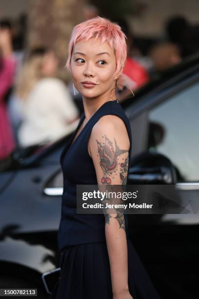 Xiaorui Kong is seen wearing gold heart big earrings, navy blue vest, plisee matching mini skirt and Ami Paris gold and black leather bag outside Ami...