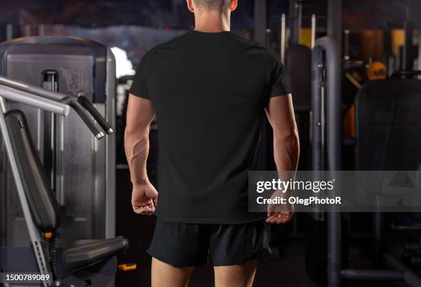 Mockup of a black t-shirt on a muscular guy against the background of equipment in the gym, rear view.