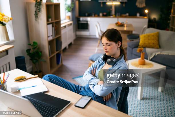 teenage girl looking at the phone in anticipation while sitting at her study desk at home - sulking stock pictures, royalty-free photos & images