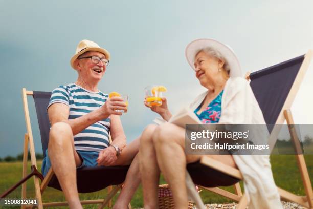 senior couple enjoying summer time, sitting on deck chairs near water. - liegestuhl stock-fotos und bilder