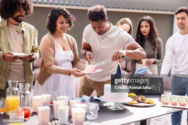 mother-to-be and her husband giving pieces of cake to the gender reveal party guests - outdoor baby shower stock pictures, royalty-free photos & images