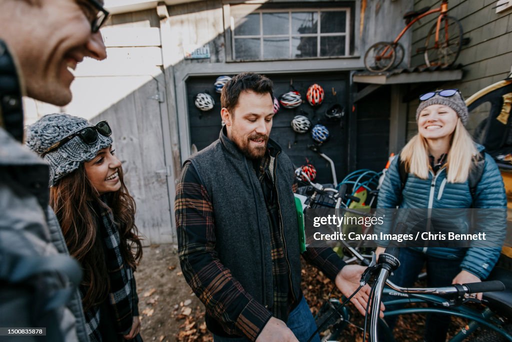 A group of young friends laughs while looking at bicycles to rent