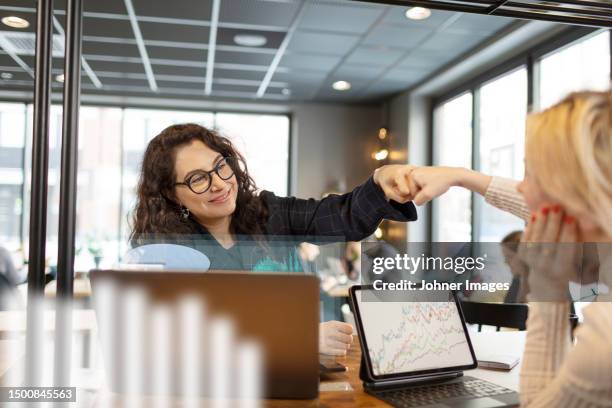 smiling woman giving fist bump to colleagues in office - fist bump stock pictures, royalty-free photos & images
