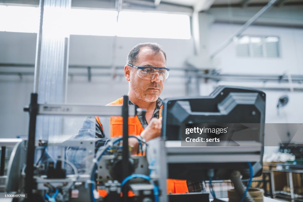 Male industrial worker working with manufacturing equipment in a factory