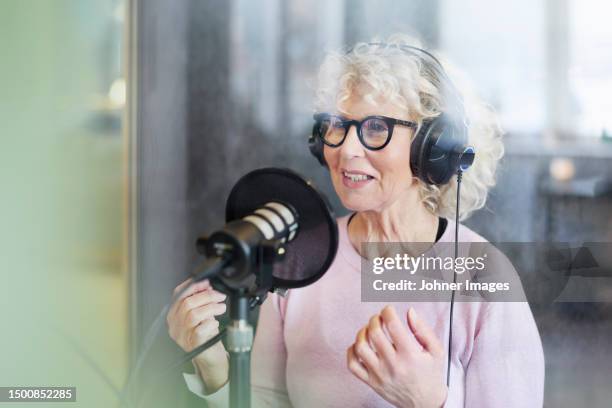 mature woman sitting and hosting podcast or radio show or podcast - mike mature stock pictures, royalty-free photos & images