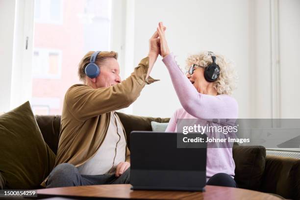 senior man and woman giving each other high five while sitting in living room in front of digital tablet - journalist computer stock pictures, royalty-free photos & images