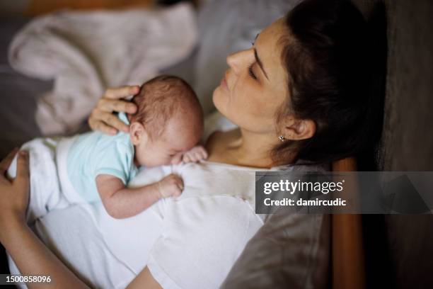 exhausted mother holding her crying newborn baby. postpartum depression. - moms crying in bed stock pictures, royalty-free photos & images