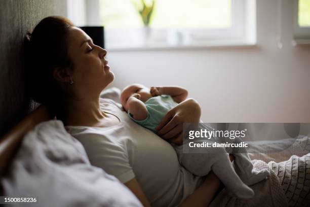 tired mother lying in bed with her newborn baby - distraught mother stock pictures, royalty-free photos & images