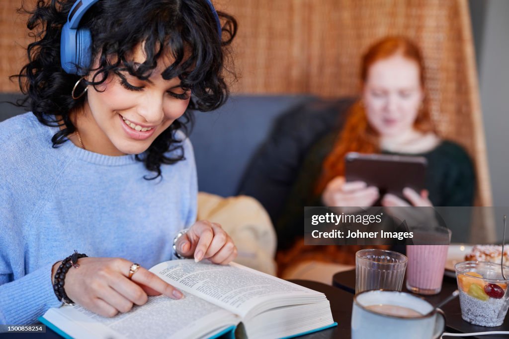 Young woman with dark curly hair with headphones reading book
