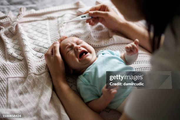 mother checking body temperature of her crying baby with a thermometer - moms crying in bed stockfoto's en -beelden