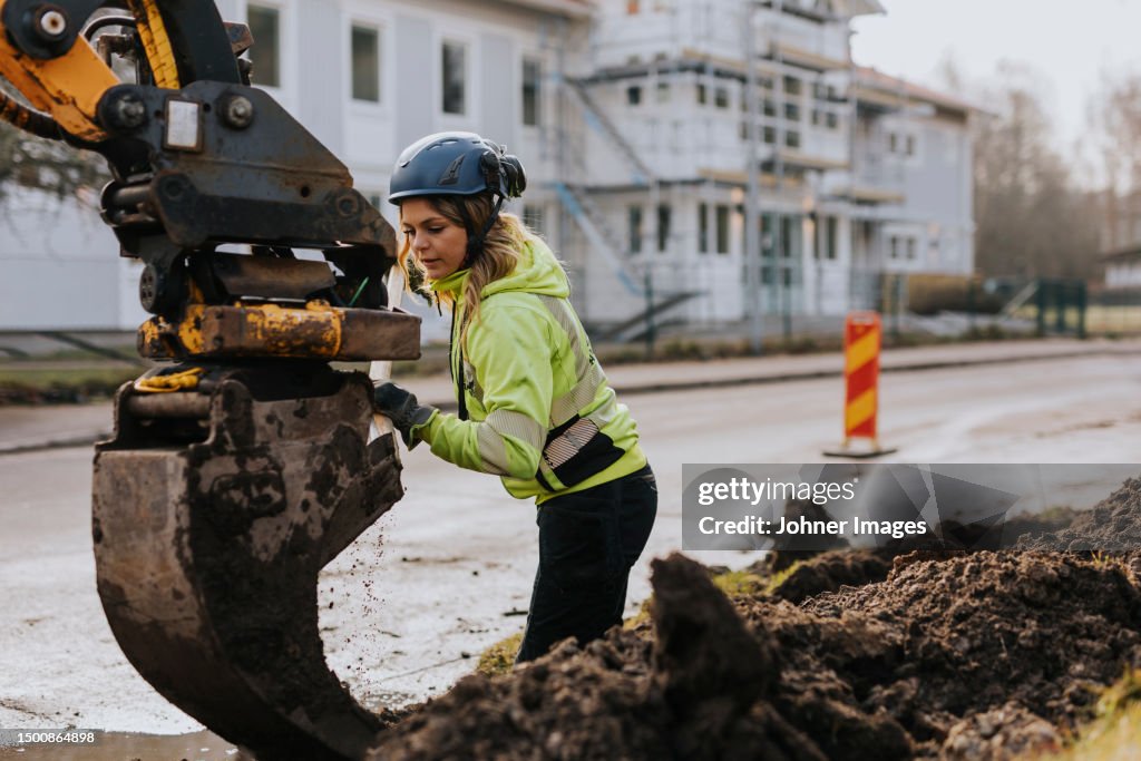 Female road worker and excavator at digging site