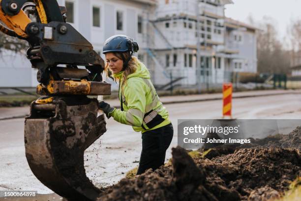 female road worker and excavator at digging site - estereotipo-de-géneros fotografías e imágenes de stock