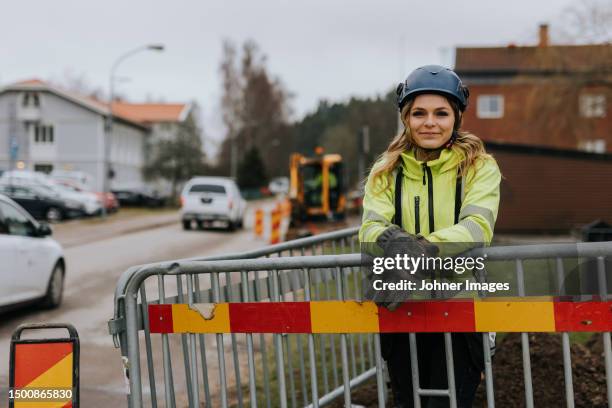 portrait of female road worker leaning against traffic barrier - construction worker pose stock pictures, royalty-free photos & images