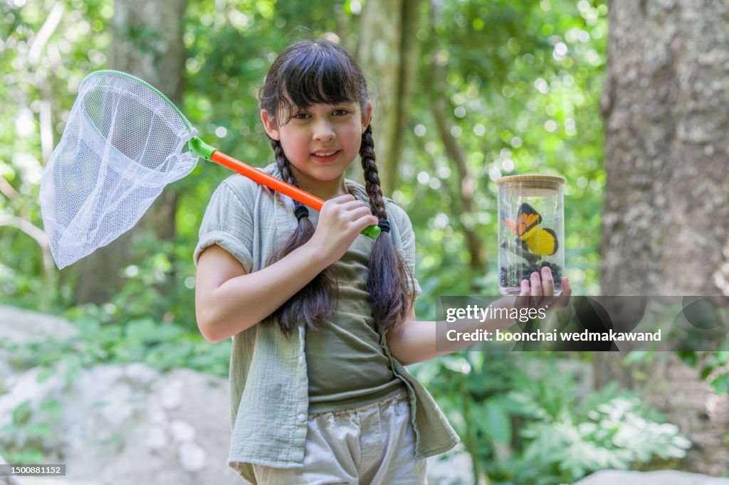 Girl with butterly in a jar in forest.